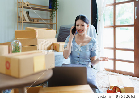 Starting small business entrepreneur of independent Asian female online seller talking on the phone with a customer and packing products for delivery to the customer. and SME delivery concept. 97592663