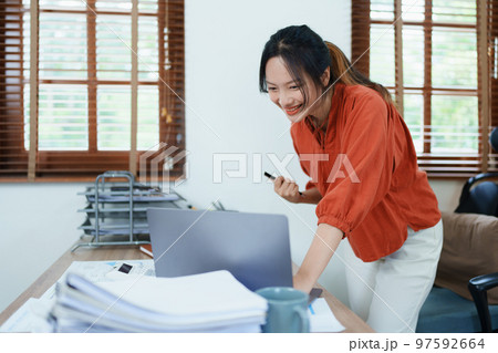 Portrait of a woman business owner showing a happy smiling face as he has successfully invested her business using computers and financial budget documents at work. 97592664