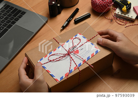 Hands holding gift box with greeting card, preparing present for family during holiday season Hands holding gift box with greeting card, preparing present for family during holiday season 97593039