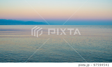The surface of the water in the Issyk Kul mountain lake in Kyrgyzstan at sunset.Pastel and soft tones of water and sky against the background of mountains. 97594541