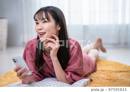カーペットに寝転んでスマホを使う若い女性 カーペットに寝転んでスマホを使う若い女性 97595833