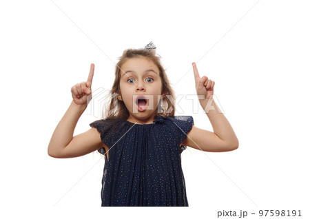 Isolated portrait on white background of a nice cheerful lovely cheery baby girl, in elegant navy dress, pointing forefinger up, finding solution, posing with open mouth and surprised look solution 97598191