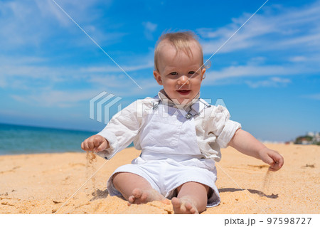 Little happy barefoot boy child sits on the beach and plays with sand on a sunny day. Little happy barefoot boy child sits on the beach and plays with sand on a sunny day. 97598727