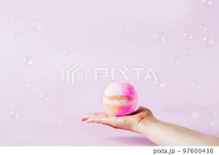 Spa concept. Pink bath bomb on the female hand on pink background with flying soap bubbles. Selective focus, copy space. 97600436