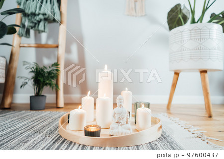 Wooden tray with burning candles and white Buddha statuette on the floor of modern Scandi interior. Zen Composition for meditation, yoga practice, relaxation. Balance and calm energy flow indoor Wooden tray with burning candles and white Buddha statuette on the floor of modern Scandi interior. Zen Composition for meditation, yoga practice, relaxation. Balance and calm energy flow indoor 97600437