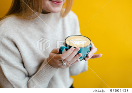Closeup shot of an unrecognizable woman hands with latte at city cafe on a yellow background Closeup shot of an unrecognizable woman hands with latte at city cafe on a yellow background 97602433