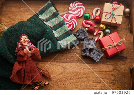 The Befana with sweet coal and candy on wooden background. Italian Epiphany day tradition. The Befana with sweet coal and candy on wooden background. Italian Epiphany day tradition. 97603926