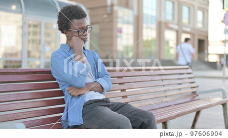 Tired Young African Man Sleeping while Sitting Outdoor on Bench 97606904