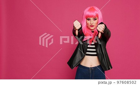 Happy beautiful adult showing thumbs down gesture in studio, showing disapproval and disappointment. Trendy stylish girl with leather jacket doing dislike bad symbol, negative disagree gesture. 97608502