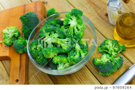 Fresh chopped broccoli in glass bowl with knife, salt and olive oil 97609264