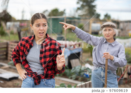 Two angry casual women neighbors of different ages arguing during the vegetable garden season on sunny day of spring Two angry casual women neighbors of different ages arguing during the vegetable garden season on sunny day of spring 97609619