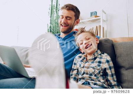Father and son sitting on couch and watching something on laptop 97609628