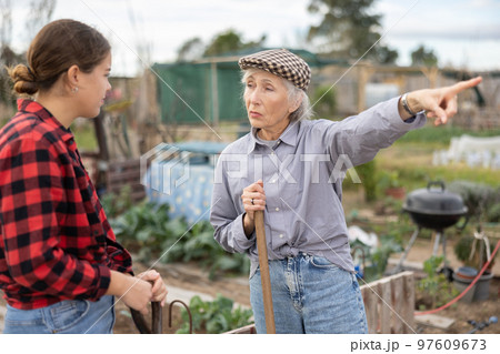 Two upset young and old female neighbors disagree with each other while digging garden on smallholding in autumn Two upset young and old female neighbors disagree with each other while digging garden on smallholding in autumn 97609673
