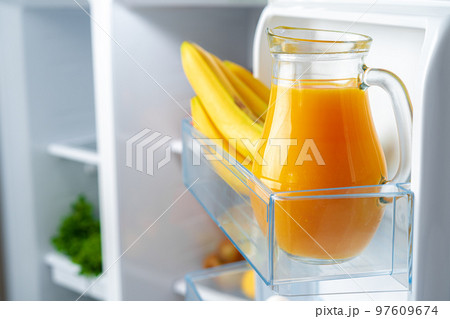 Glass pitcher of orange juice and fruits on fridge shelf 97609674