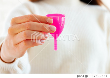 Woman in white sweater holding pink menstrual cup in hands close up Woman in white sweater holding pink menstrual cup in hands close up 97609684
