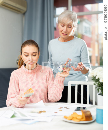 Young woman holding out banknotes to aged mother at home table 97609890