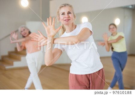 Woman dancing modern dance with other women during group training in classroom Woman dancing modern dance with other women during group training in classroom 97610188