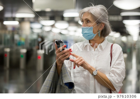 Caucasian woman in mask with smartphone in subway station 97610306