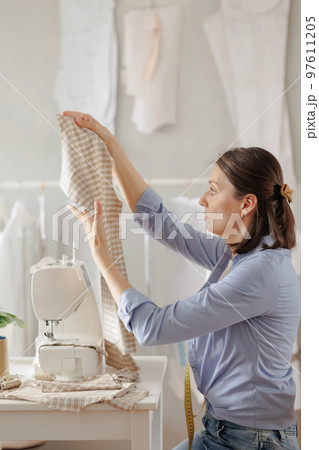 woman seamstress in workshop sews clothes for sale. cozy workplace, small business or hobby 97611205