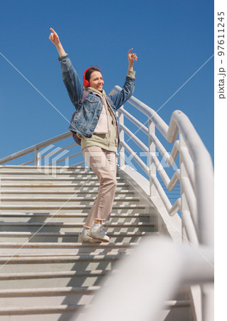 woman dances and sings on stairs, listens to music or podcast with red headphones, full-length woman dances and sings on stairs, listens to music or podcast with red headphones, full-length 97611245