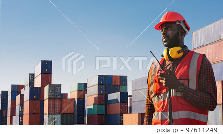 American African engineer or factory worker man using walkie talkie and check up goods at container cargo harbor. American African engineer or factory worker man using walkie talkie and check up goods at container cargo harbor. 97611249