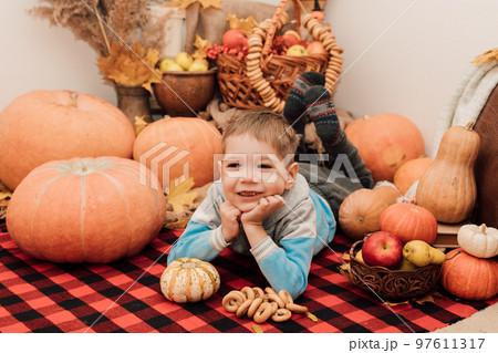 A little boy lies on the floor near pumpkins and autumn fruits. Autumn Festival A little boy lies on the floor near pumpkins and autumn fruits. Autumn Festival 97611317