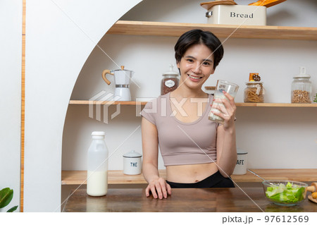 Asian young beautiful woman drinking glass of milk in kitchen at home. health care concept 97612569