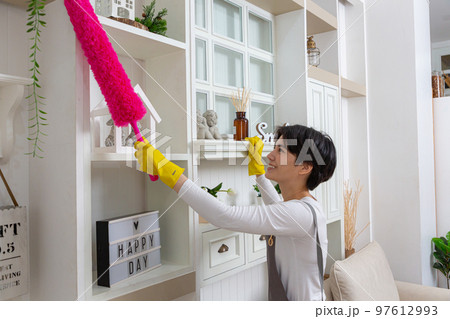 Woman cleaning dust from bookshelf. Young girl sweeping shelf in living room. 97612993