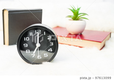 Black alarm clock and book stacked on table Black alarm clock and book stacked on table 97613099