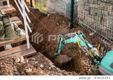 Mini excavator digs a trench to lay pipes. Close up of an excavator digging a deep trench. An excavator digs a trench in the countryside to lay a water pipe. Slow motion 97614341