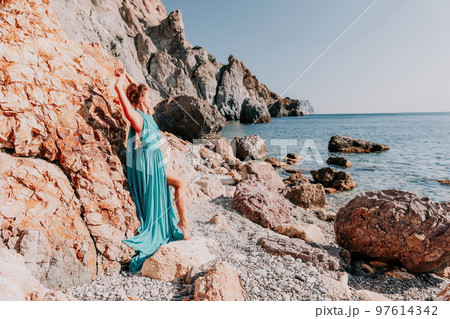 Side view a Young beautiful sensual woman with black hair in a long mint dress posing on a beach with calm sea bokeh lights on sunny day. Girl on the nature on blue sky background. Fashion photo 97614342