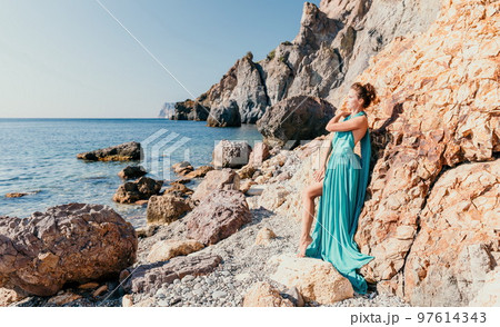 Side view a Young beautiful sensual woman with black hair in a long mint dress posing on a beach with calm sea bokeh lights on sunny day. Girl on the nature on blue sky background. Fashion photo Side view a Young beautiful sensual woman with black hair in a long mint dress posing on a beach with calm sea bokeh lights on sunny day. Girl on the nature on blue sky background. Fashion photo 97614343