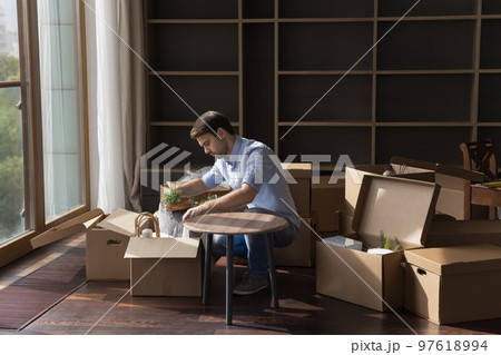 Serious young renter man unpacking stuff, moving into new apartment Serious young renter man unpacking stuff, moving into new apartment 97618994