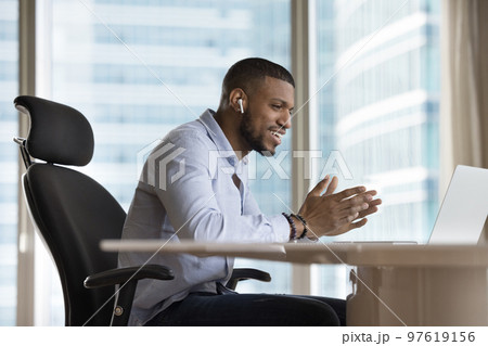 Happy businessman with earbud in ear talking on video call Happy businessman with earbud in ear talking on video call 97619156