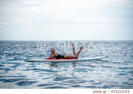 Woman sap sea. Sports girl on a surfboard in the sea on a sunny summer day. In a black bathing suit, he lies on a sap in the sea. Rest on the sea. 97620293