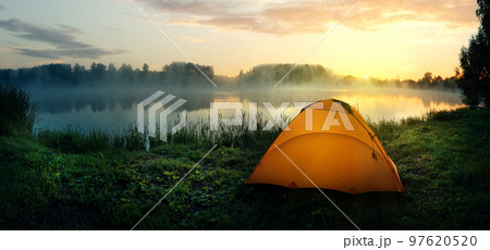 Orange tent on the bank of the river covered with fog in early morning Orange tent on the bank of the river covered with fog in early morning 97620520