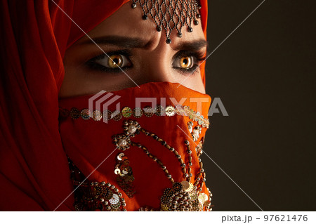 Studio shot of a young charming woman wearing the terracotta hijab decorated with sequins and jewelry. Arabic style. 97621476