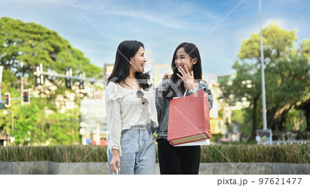 Image of two young asian women talking, spending time together while walking in the shopping district of a city 97621477