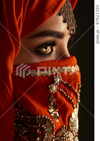 Studio shot of a young charming woman wearing the terracotta hijab decorated with sequins and jewelry. Arabic style. 97621503