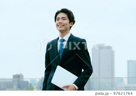 屋上でパソコンを持って立つビジネスマン 97621764