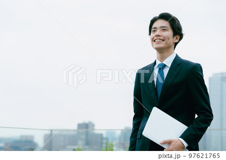 屋上でパソコンを持って立つビジネスマン 97621765