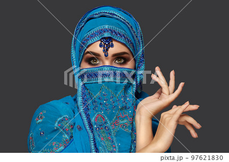 Studio shot of a young beautiful woman wearing the blue hijab decorated with sequins and jewelry. Arabic style. 97621830