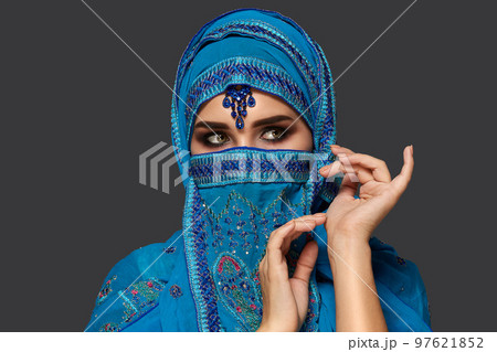 Studio shot of a young beautiful woman wearing the blue hijab decorated with sequins and jewelry. Arabic style. 97621852