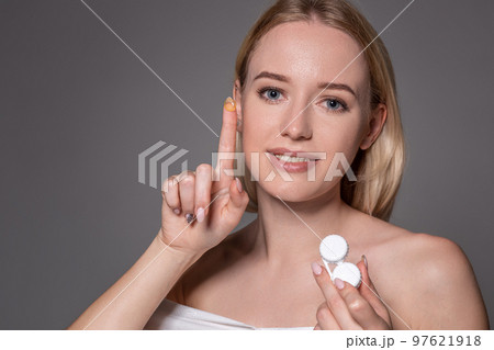 Portrait of young beautiful woman with natural makeup and contact eye lens in hand. Close-up of female model holding white lens box. Portrait of young beautiful woman with natural makeup and contact eye lens in hand. Close-up of female model holding white lens box. 97621918