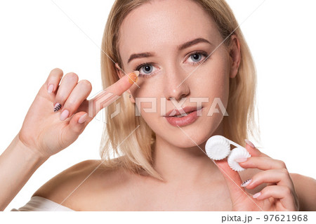 Young woman holding contact lenses cases and lens in front of her face on white background Young woman holding contact lenses cases and lens in front of her face on white background 97621968