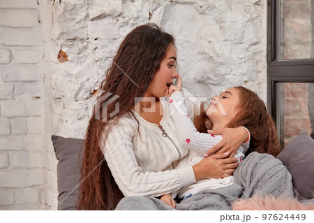 Mother and daughter sitting on sill near window in room 97624449