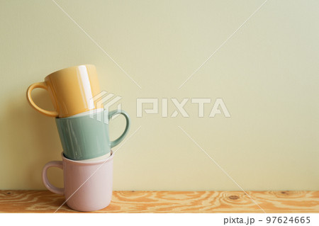 Stack of pastel color mug cups on wooden table. ivory wall background. kitchen and cafe concept 97624665