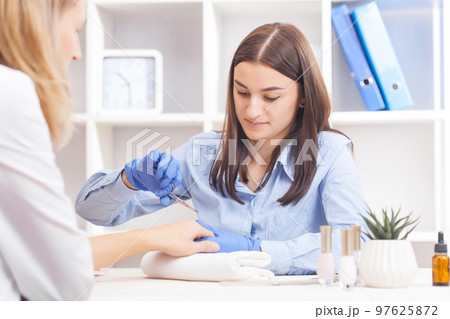 finger nail care by manicure specialist in beauty salon. Manicurist clear cuticle with professional scissors for manicure 97625872