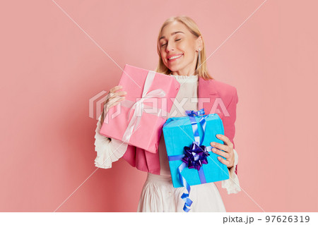 Portrait of beautiful, stylish woman emotionally posing with present boxes over pink background Portrait of beautiful, stylish woman emotionally posing with present boxes over pink background 97626319