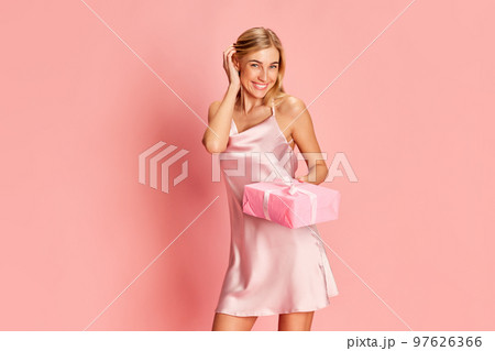 Portrait of beautiful young woman posing in teder silk dress over pink background. Receiving presents. Holidays, celebration and women concept 97626366